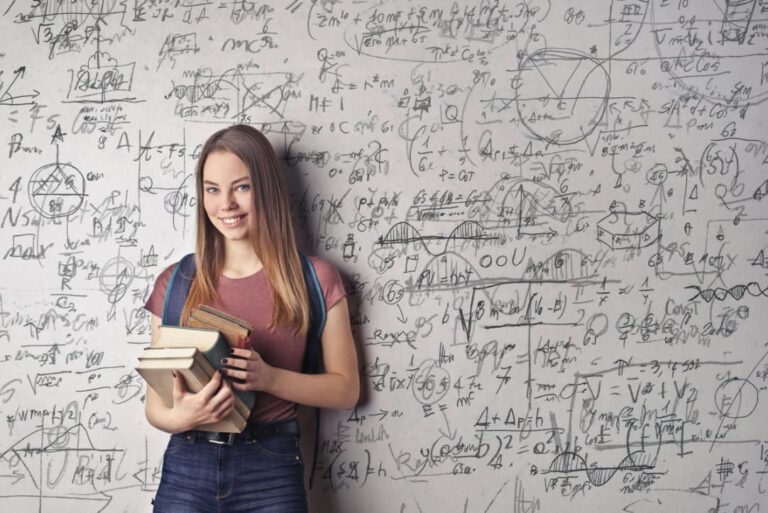 A woman standing in front of a wall covered with handwritten physics equations