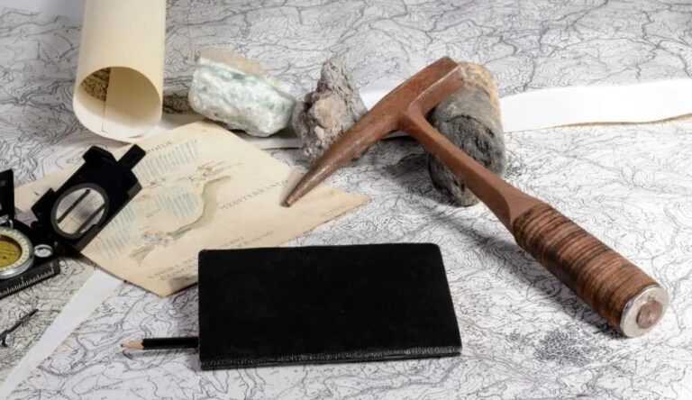 A geologist's workspace with a map, hand lens, hammer, notebook, pencil, and rock samples