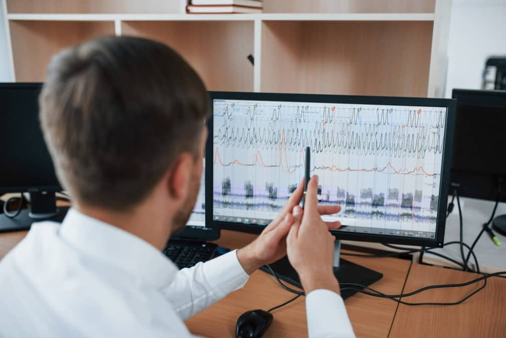 An individual analyzing complex graphs on multiple computer monitors