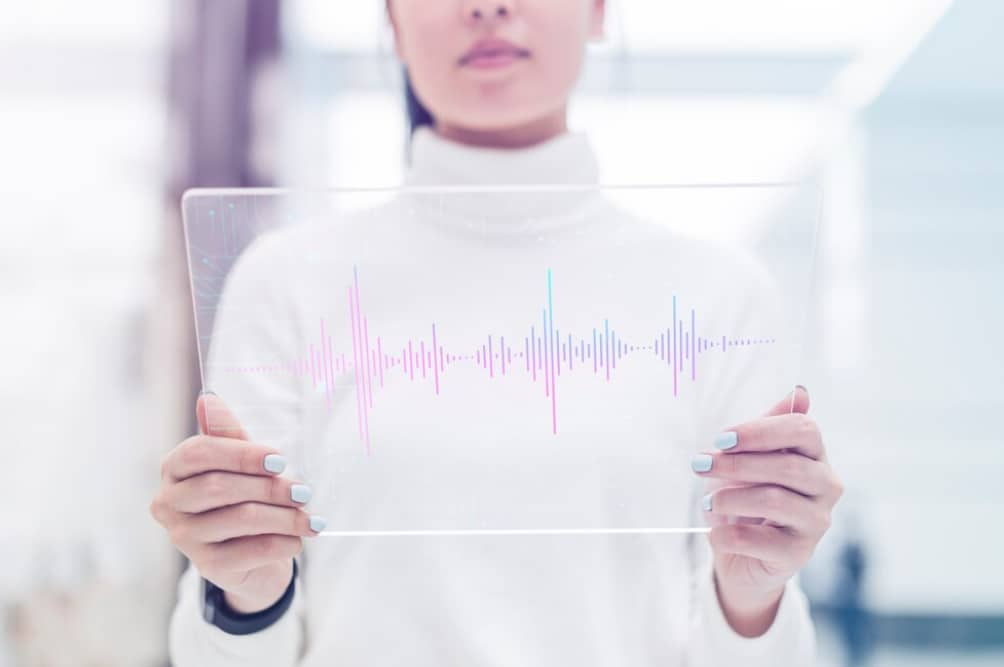 A person holds a clear tablet displaying a colorful audio waveform