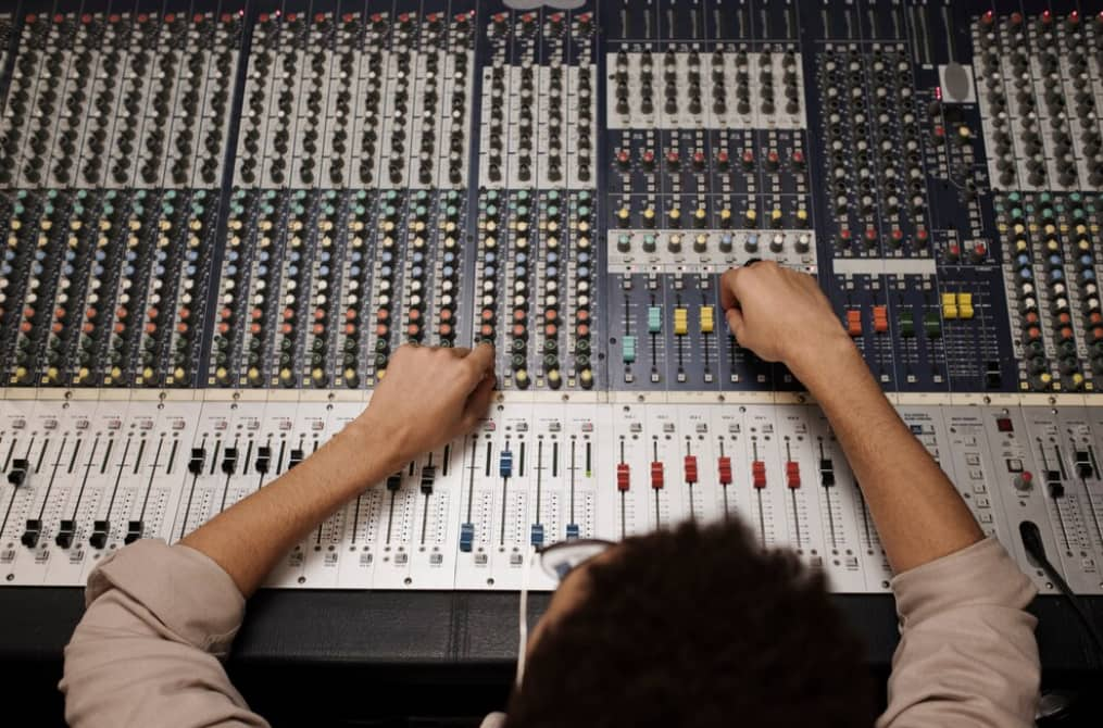 Hands adjusting knobs on a complex audio mixing console