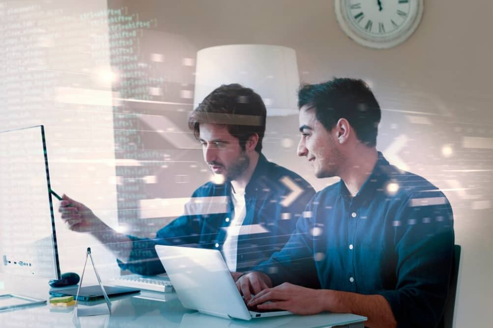 Two men focused on coding and discussing in front of computers